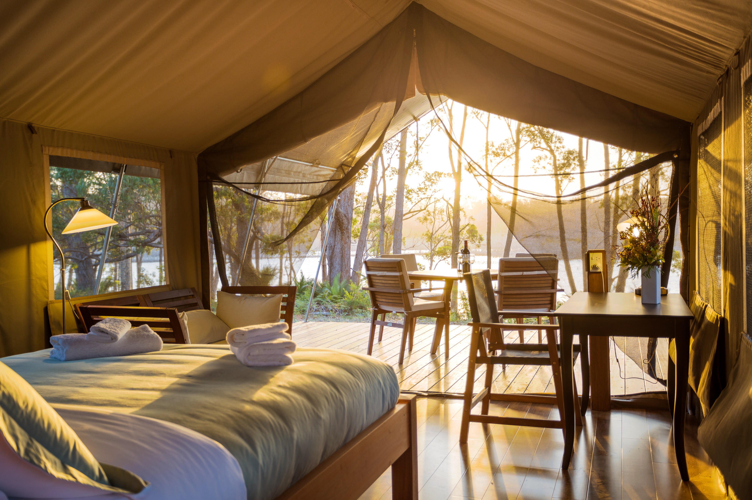 Inside a luxury safari tent with queen bed, writing desk and deck overlooking bush and lagoon at sunset